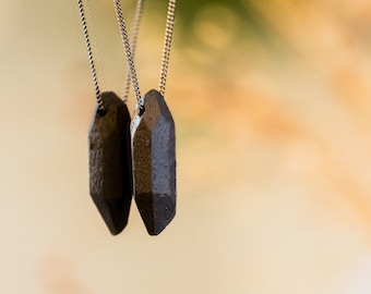 May include: Two silver chains with dark grey, geometric pendant charms hanging from them. The charms are shaped like elongated, pointed crystals.