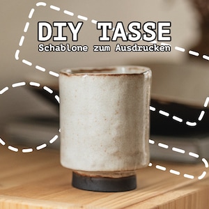 May include: A white ceramic mug with a dark brown rim and base. The mug is sitting on a wooden surface. The text "DIY TASSE Schablone zum Ausdrucken" is written in white on a white background with a dashed line border.