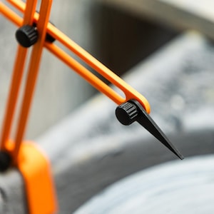 May include: Close-up of an orange and black compass tool. The tool has a bright orange frame with black adjustment knobs and a black pointed tip. The tool is designed for precise measurements and drawing circles.