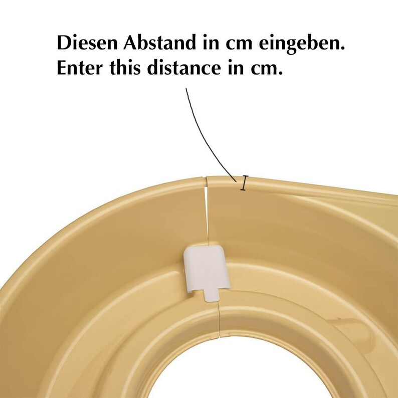 May include: A close-up of a tan-colored plastic object with a curved design. The text "Diesen Abstand in cm eingeben. Enter this distance in cm." is visible in the image. A white plastic piece is attached to the object.