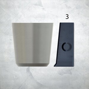 May include: A gray ceramic cup and a black plastic cup holder with a round hole in the center. The cup holder has the number "3" printed on it.