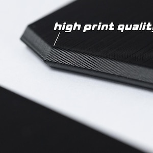 May include: Close-up of a black 3D printed object with a smooth, textured surface. The object has a sharp, defined edge. The text "high print quality" is visible in the image.
