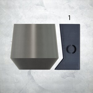May include: Two gray metal bottle stoppers, one with a round top and the other with a flat top. The flat top stopper has a circular cutout.