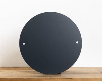 May include: A dark grey round metal sign with two small holes for hanging. The sign is blank and ready to be customised.