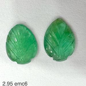 Può includere: Due pietre preziose di smeraldo scolpite a forma di foglie. Le pietre preziose sono di un colore verde vibrante con venature dettagliate. Il testo "2.95 emc6" è in basso nell'immagine.