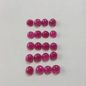 Peut inclure: Quinze pierres précieuses rondes, polies, taillées en cabochon, d'une teinte magenta vibrante, sont disposées en cinq rangées de trois. Les pierres sont espacées uniformément sur un fond blanc, mettant en valeur leurs surfaces lisses et brillantes.