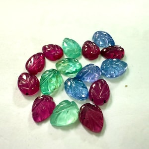May include: A collection of gemstone leaf carvings in various colors, including ruby red, emerald green, and shades of blue. Each leaf-shaped stone is intricately carved with detailed veining, creating a naturalistic appearance. The gemstones are arranged on a white surface.