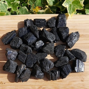 May include: A collection of tumbled black tourmaline stones. The stones are of various sizes and shapes, with some showing a striated pattern.