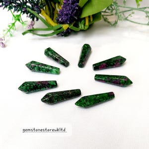 May include: Eight green and pink gemstone points, also known as ruby zoisite, arranged in a circle on a white surface. The points are all approximately the same size and shape, and they have a smooth, polished finish.