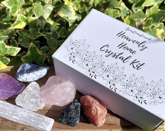 May include: A white box with black text that reads "Heavenly Home Crystal Kit" and a floral design. The box is open and contains a variety of crystals, including amethyst, rose quartz, clear quartz, selenite, and blue lace agate.
