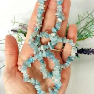 K&ouml;nnte beinhalten: Eine Halskette aus kleinen, unregelm&auml;&szlig;igen Aquamarin-Edelsteinen. Die hellblauen und wei&szlig;en Steine sind zu einem zarten Strang aufgereiht. Die Halskette wird vor einem hellen Hintergrund mit einem Hauch von Gr&uuml;n pr&auml;sentiert.