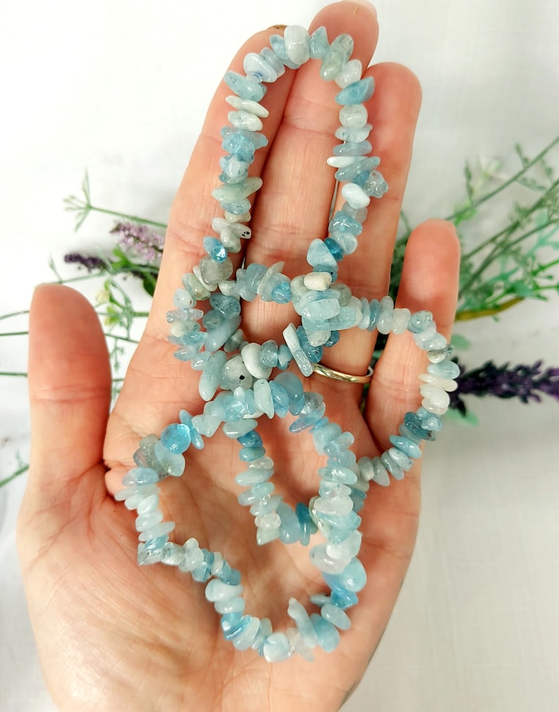 K&ouml;nnte beinhalten: Eine Halskette aus kleinen, unregelm&auml;&szlig;igen Aquamarin-Edelsteinen. Die hellblauen und wei&szlig;en Steine sind zu einem zarten Strang aufgereiht. Die Halskette wird vor einem hellen Hintergrund mit einem Hauch von Gr&uuml;n pr&auml;sentiert.