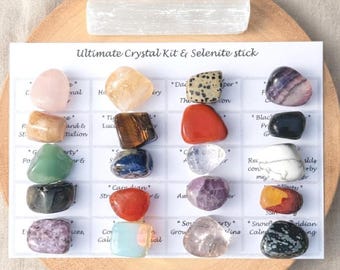 May include: A collection of sixteen polished tumbled gemstones arranged in a four-by-four grid on a white card labelled Ultimate Crystal Kit & Selenite stick, accompanied by a single rectangular white selenite stick placed at the top.