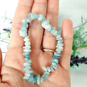 K&ouml;nnte beinhalten: Ein Armband aus kleinen, unregelm&auml;&szlig;igen aquamarinfarbenen Steinen. Die Steine sind zu einem flexiblen Band aufgereiht. Das Armband hat eine hellblaue Farbe mit Farbvariationen. Das Armband wird in einer Hand gehalten.