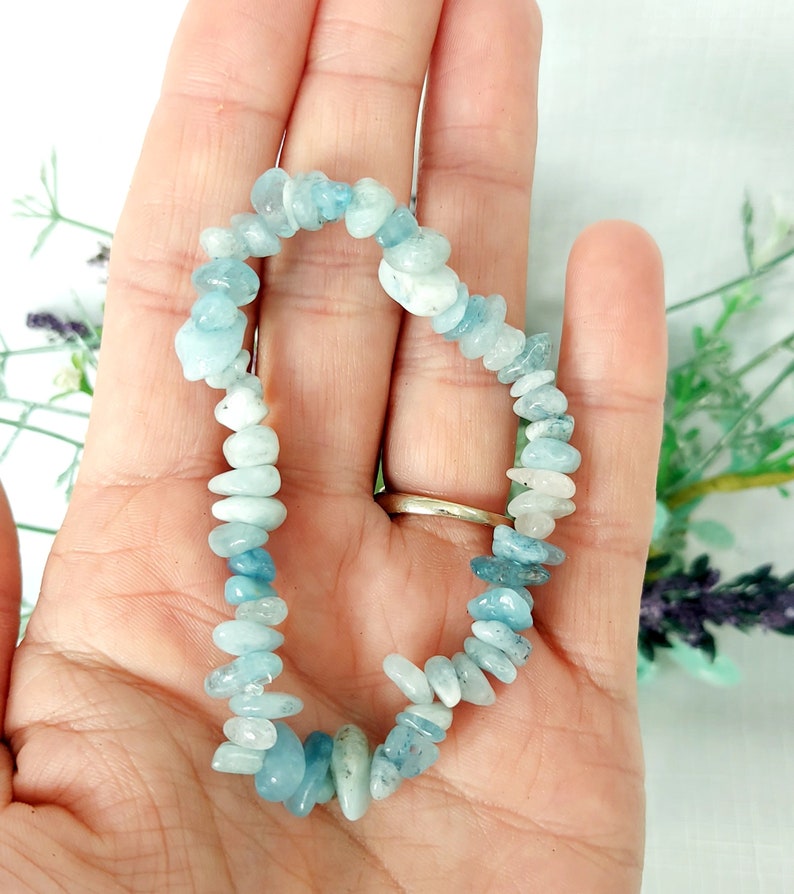 K&ouml;nnte beinhalten: Ein Armband aus kleinen, unregelm&auml;&szlig;igen aquamarinfarbenen Steinen. Die Steine sind zu einem flexiblen Band aufgereiht. Das Armband hat eine hellblaue Farbe mit Farbvariationen. Das Armband wird in einer Hand gehalten.