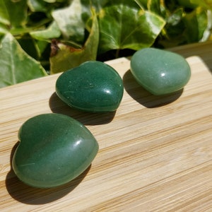 Pu&ograve; includere: Tre pietre verdi a forma di cuore su una superficie di legno. Le pietre hanno una consistenza lucida e liscia e variano leggermente nella tonalit&agrave;. Lo sfondo presenta un fogliame verde, aggiungendo un elemento naturale alla composizione.