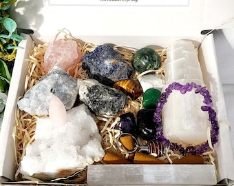 May include: A white box filled with various crystals and stones, including rose quartz, tiger eye, serpentine, amethyst, and carnelian. The box also includes a white selenite wand, a selenite charging plate, and a selenite bracelet. The box is labeled with the text "gemstonestoreukltd".