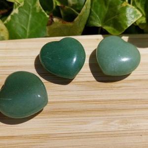 Pu&ograve; includere: Tre pietre verdi a forma di cuore su una superficie di legno. Le pietre variano in tonalit&agrave; dal verde scuro al verde chiaro. La superficie in legno presenta un motivo a venature naturali. Sullo sfondo sono visibili foglie verdi.