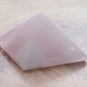 May include: A light pink and white triangular shaped cabochon gemstone.