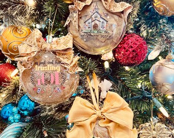 May include: Christmas tree ornaments with gold glitter, bows, and inspirational messages. One ornament features a church illustration with the text "consider how the wildflowers grow." Another says "I'm just out here trusting GOD." The third says "Make Heaven Crowded."