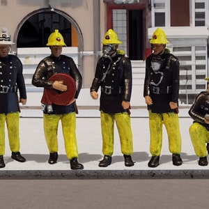 May include: Five miniature firefighters wearing yellow helmets and black jackets with yellow trousers. The firefighters are holding hoses and other firefighting equipment.