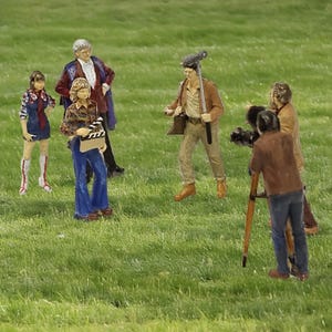 May include: A collection of miniature film crew figurines set on a grassy surface. The scene features a director with a clapperboard, a cameraman with a tripod, and other crew members. The figures are dressed in retro clothing, suggesting a vintage theme.