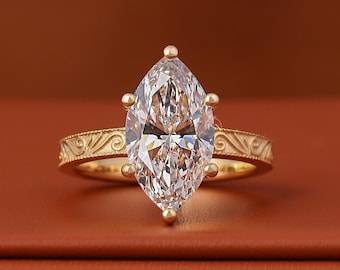 May include: A gold ring featuring a large, clear marquise-cut gemstone held by six prongs. The band is crafted from yellow gold and displays an intricate, raised scrollwork pattern along its entire outer surface, providing a textured finish.