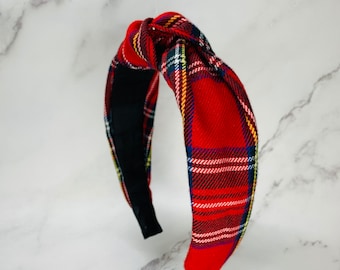 May include: A knotted headband featuring a red, black, white, and yellow plaid pattern. The fabric is wrapped around a structured frame, with a solid black lining visible on the inner side of the band, creating a distinct knotted detail at the top.