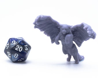 Könnte beinhalten: Eine violette 3D-gedruckte Miniatur einer geflügelten Kreatur mit einem langen Schwanz, die auf einer weißen Oberfläche steht. Ein blauer und silberner 20-seitiger Würfel befindet sich im Vordergrund.