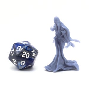 Puede incluir: Un dado de 20 caras de color azul y negro con números blancos y una figura en miniatura de un fantasma de color gris y blanco.