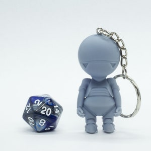 Puede incluir: Un llavero de robot gris con una cadena plateada y un dado de 20 caras azul y plateado.