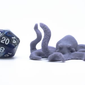 May include: A purple 3D printed octopus figurine with eight tentacles. The octopus is lying on its side with its tentacles spread out. A blue and silver 20-sided die is in the background.
