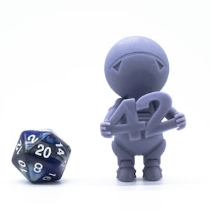 Puede incluir: Una figurita morada sosteniendo un cartel que dice "42". Un dado de 20 caras azul y plateado está en primer plano.