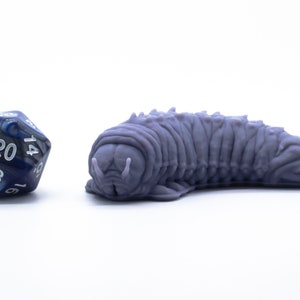 May include: A purple 3D printed creature resembling a worm with a segmented body and a pointed head. A blue and silver 20-sided die is in the foreground.