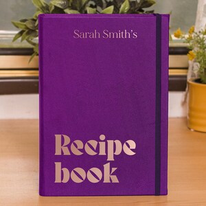 Puede incluir: Libro de recetas morado con el texto "Sarah Smith's Recipe Book" en letras doradas.