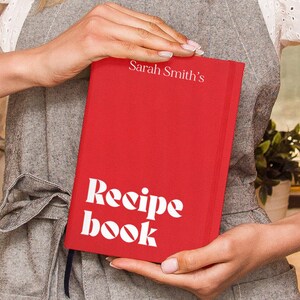 Puede incluir: Un libro de recetas de tapa dura rojo con el texto "Sarah Smith's Recipe Book" en letras blancas.