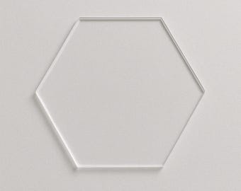 May include: A clear, hexagonal acrylic coaster with a minimalist design. The coaster is transparent and sits on a white surface, offering a modern and clean aesthetic. Ideal for protecting surfaces from drink rings.