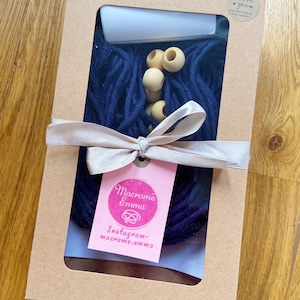 May include: A brown cardboard box with a clear window showing a navy blue macrame kit. The kit includes wooden beads, string, and a tag that says "Macrame Emma" and "Instagram - macrame.emma". The box also has a sticker that says "Thank you for supporting my small business".