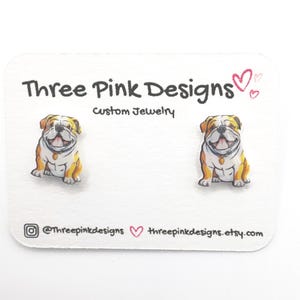 May include: A pair of bulldog earrings on a white card with the text "Three Pink Designs Custom Jewelry" and the social media handles @threepinkdesigns and threepinkdesigns.etsy.com.