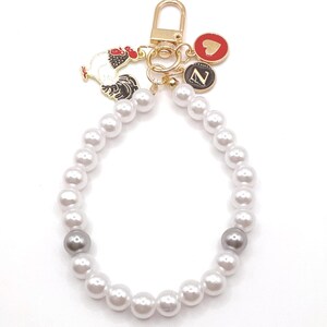 May include: A white pearl keychain with a gold metal rooster charm, a gold heart charm, and a gold charm with the letter "Z" on it.