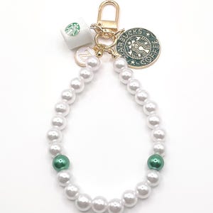 Peut inclure: Un porte-clés en perles blanches avec un charme en or qui dit "Starbucks Coffee" et un petit charme en céramique blanche avec un logo Starbucks vert. Le porte-clés a également deux accents de perles vertes.