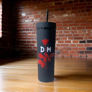 May include: Black reusable tumbler with a red rose and the letters "DM" in white. The tumbler has a black lid and a straw.