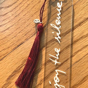 May include: A clear acrylic bookmark with a burgundy tassel. The bookmark has the words "enjoy the silence" written in white on it.