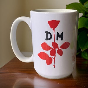 Puede incluir: Taza de cerámica blanca con una rosa roja y las letras "DM" en negro.