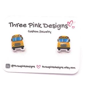 May include: A pair of yellow school bus earrings with blue windows. The earrings are on a white card with the text "Three Pink Designs Custom Jewelry" and the social media handles @threepinkdesigns and threepinkdesigns.etsy.com.
