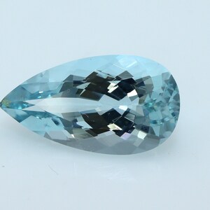 May include: A pear-shaped, faceted aquamarine gemstone. The gem is a light blue color with multiple facets that reflect light. The gemstone is set against a white background.
