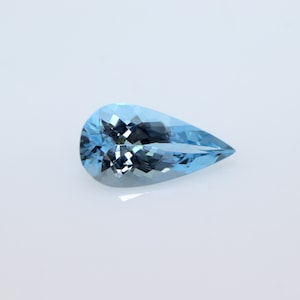 May include: A pear-shaped, faceted gemstone with a translucent, light blue color. The stone features a brilliant cut with multiple triangular and kite-shaped facets that reflect light, creating a sparkling appearance against a plain white background.