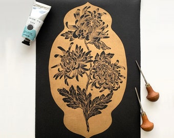 May include: A black and gold print of a floral design featuring three chrysanthemums with intricate details. The print is on a black background and is framed in a gold border.