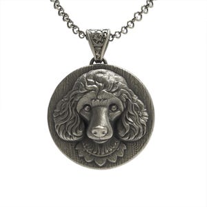 Puede incluir: Collar con colgante de plata con una imagen esculpida en tres dimensiones detallada de la cara de un caniche.