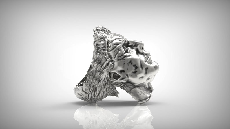 May include: A silver ring with a detailed sculpture of a person's head. The head is tilted back and the person's eyes are closed.